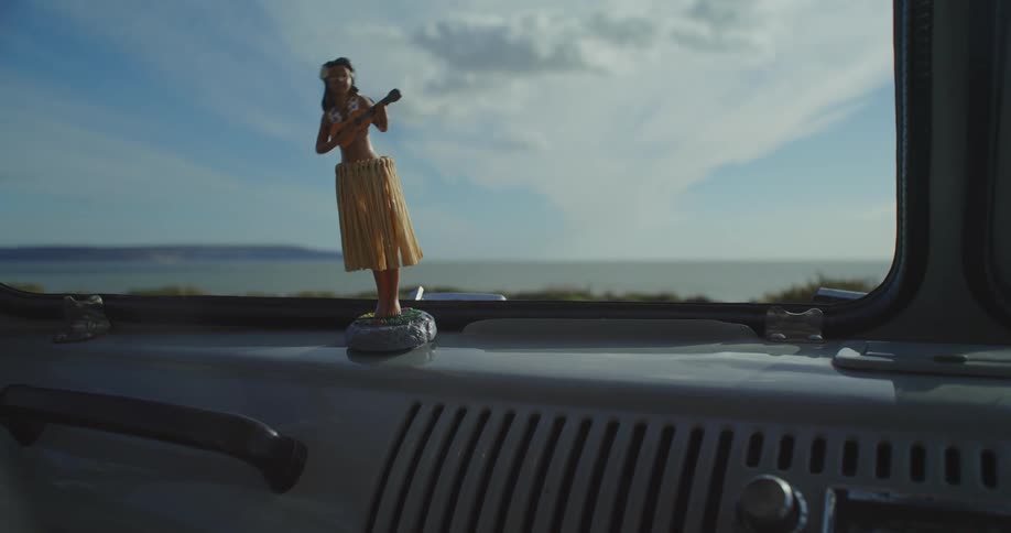 A hand pushes on a dancing hula girl doll on a classic car  dashboard