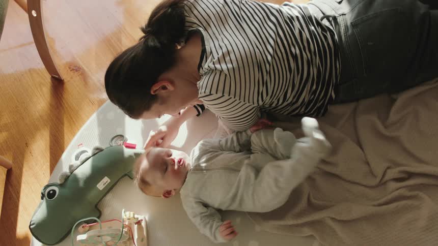 Mom lying on a mat playing with baby and the family dog