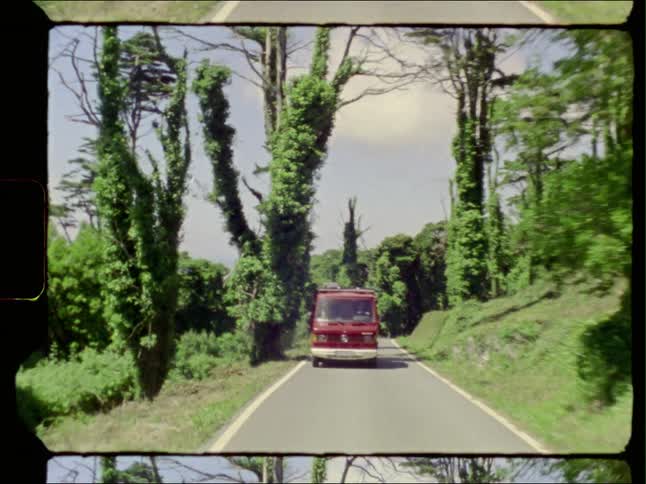 A van drives down a narrow road through a forest