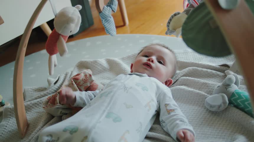 A baby is lying on a bed with toys on a mobile hanging above