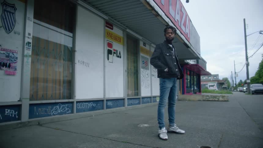 A man stands outside a business as traffic passes by