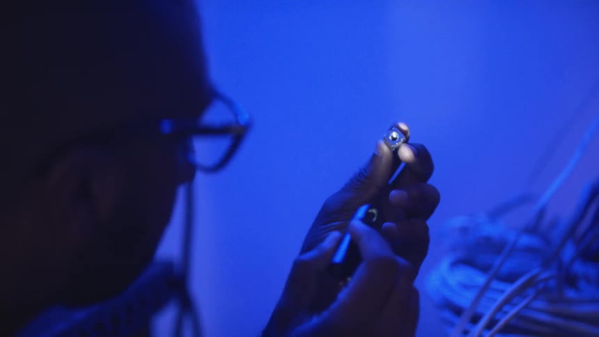 A man is holding a metal piece in his hand and examining it with a small flashlight