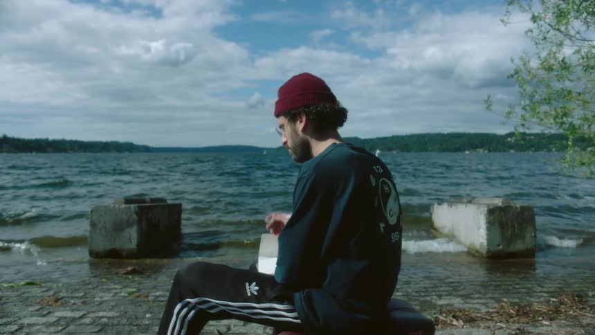 Man sitting on block on shore writes in journal as waves roll onto shore