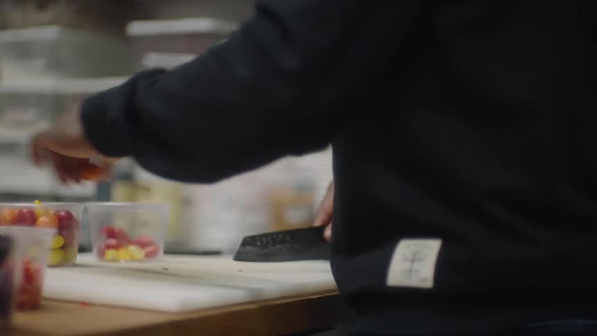 A person standing slicing grape tomatoes in half and placing in a plastic container