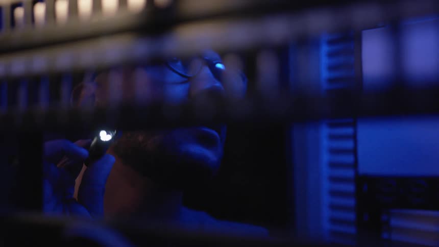 A man uses a small flashlight as he looks at shelving following wire