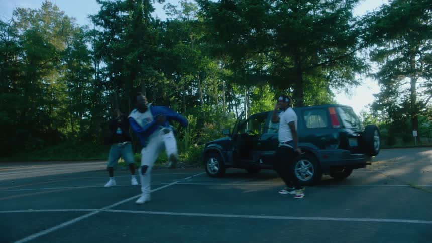 Male dancers dance next to black car in the car park