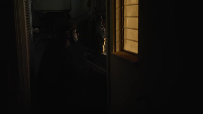 Man with glasses repairs electric panel near the window at night