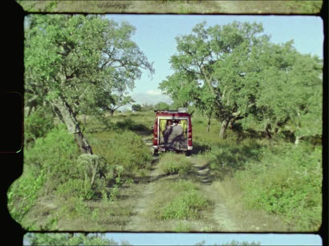 Vintage film of two people lying in the back of a van parked on a trail