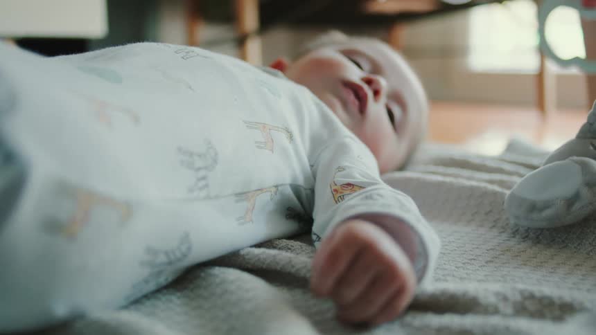 A baby lies on a blanket in a home