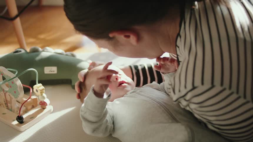 A woman is lying down next to her baby as they laugh and play together