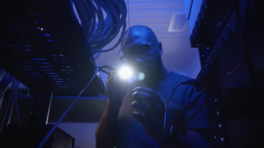 A man in a dark room shines a flashlight on a small object as he inspects it