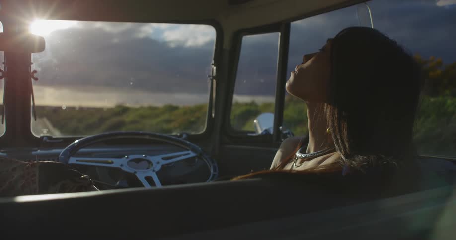 A woman sits  in a parked classic van and looks out the window at the sea