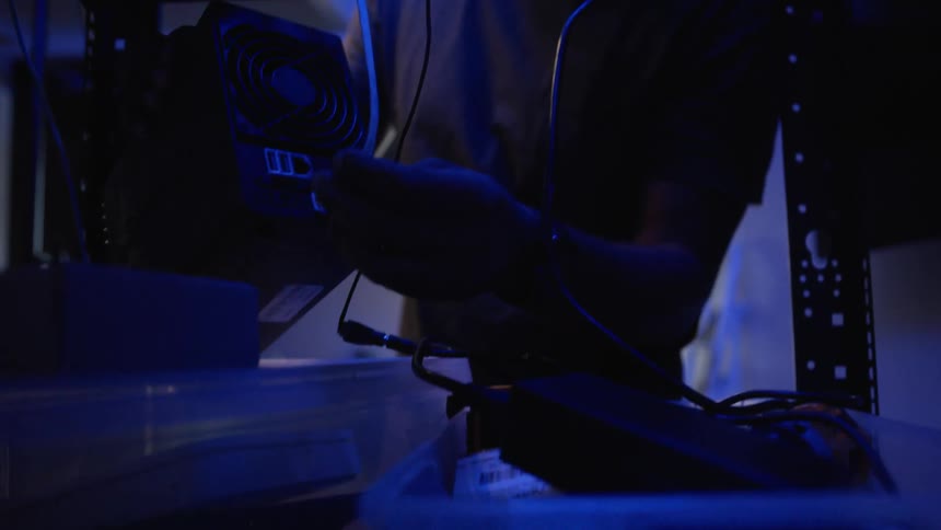 IT professional connects computer hardware in room lit by blue colored lighting