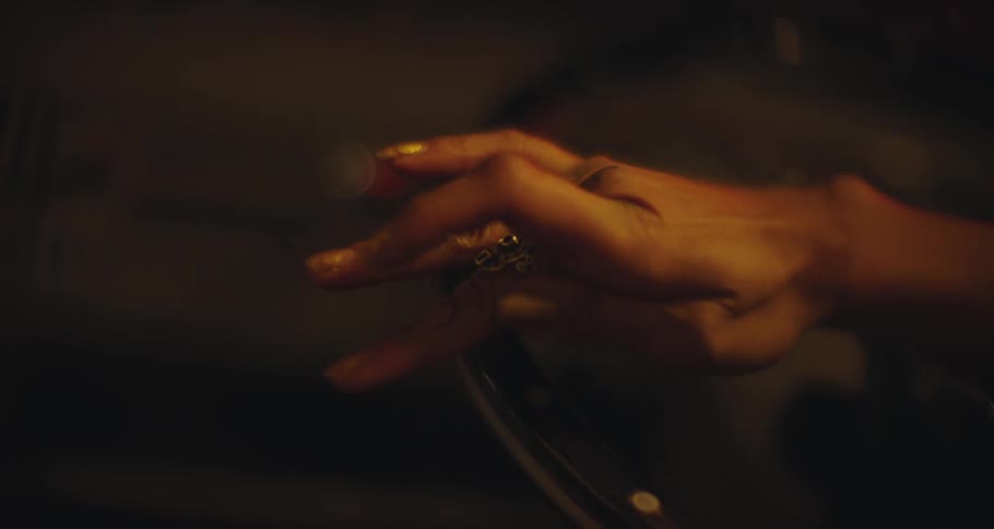 Woman wearing a ring, wiggles her tattooed fingers in a dimly lit car