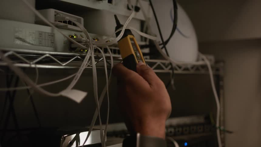 Man using a cable meter network tester to measure electronic equipment on a rack