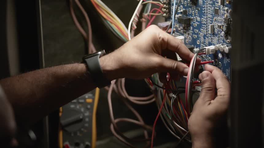 Close up of the hands of a technician testing the pins on an electronic board mounted on a rack