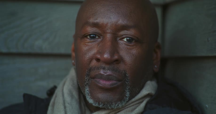 A man is sitting outdoors and smiling at the camera
