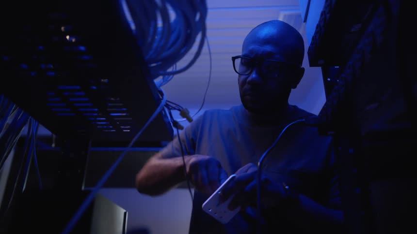 A man works on wiring a system sitting on metal shelves