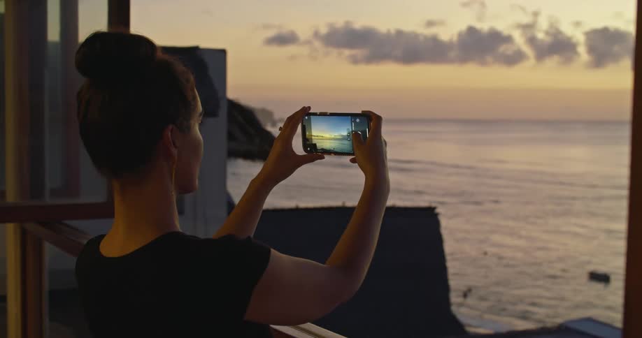 A woman using a smartphone to take photos of the ocean