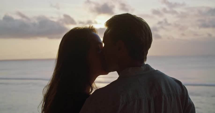 A couple kiss on the beach as they watch the sunset