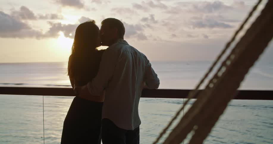A couple kiss and drink wine while watching the sun set along the coast