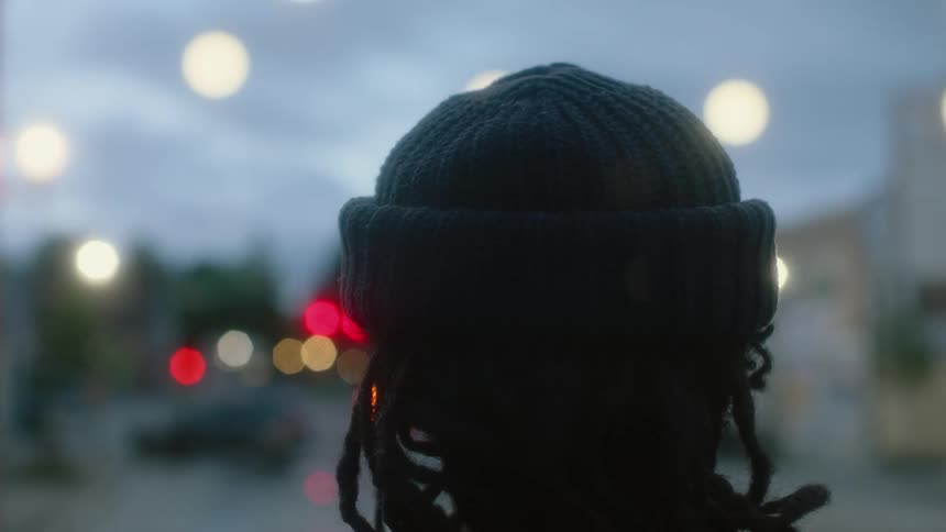 Back of the head of a person with dreadlocks wearing a cap looking at a street in a small town