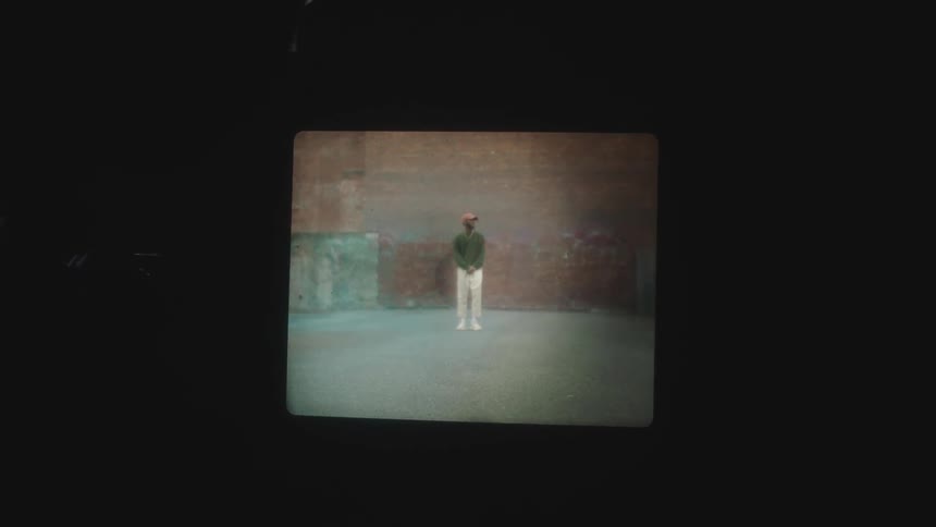 Film projected on a dark room of a man standing still in front of a brick wall
