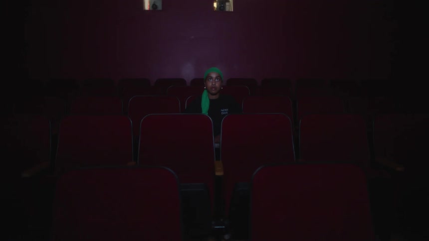 A teenage male is sitting alone in a movie theater staring intently at something
