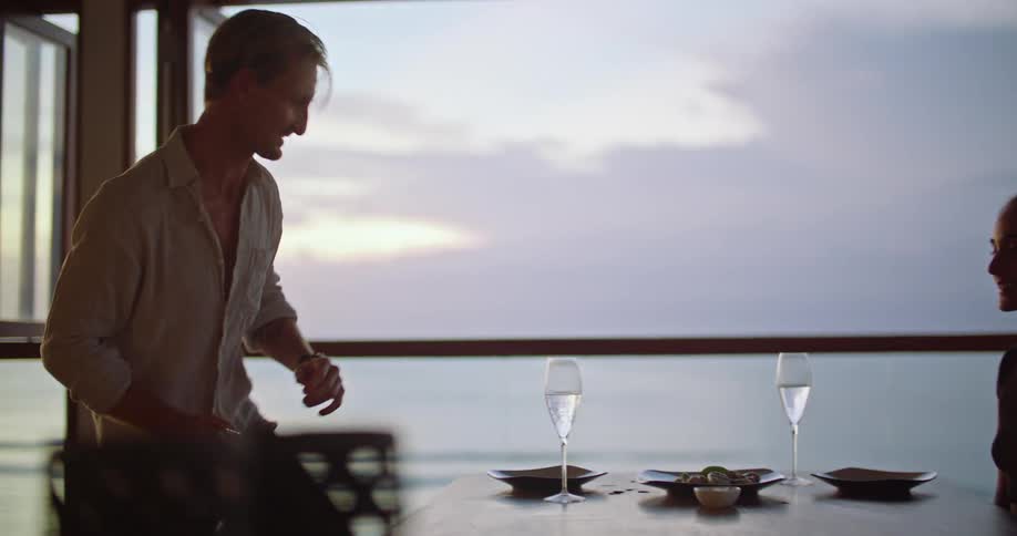 A man places a dish with food on a table and sits with his female companion