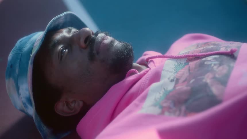 Man wearing blue hat and pink hoodie lies on the ground