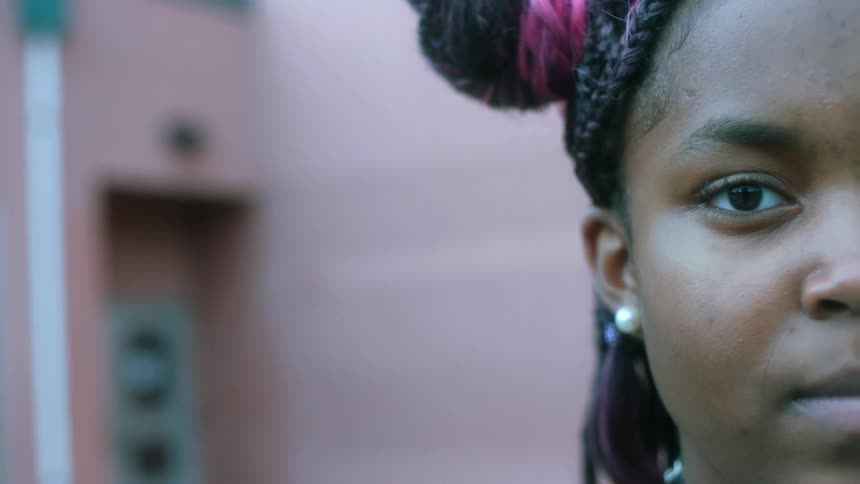 The face of a teenage black girl standing outside looking straight ahead