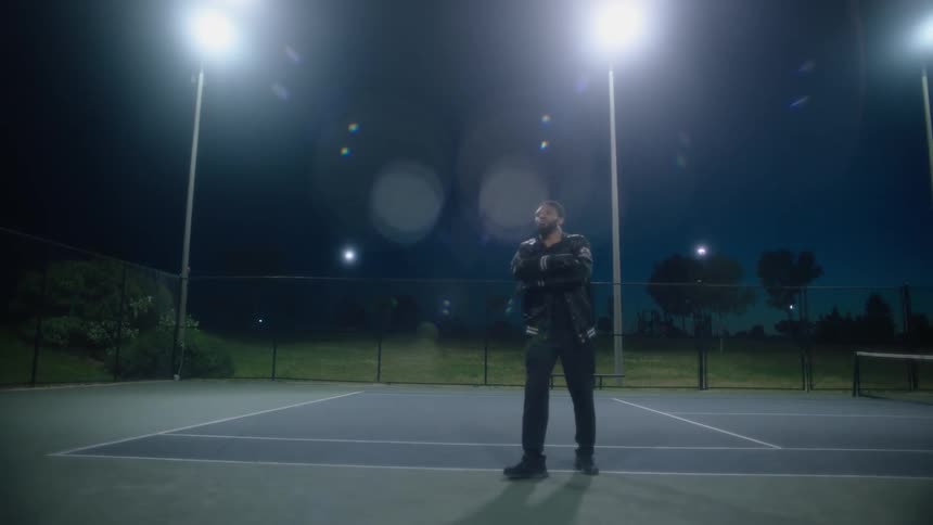 Man with black leather jacket shirt and pants warms up his arms on the court