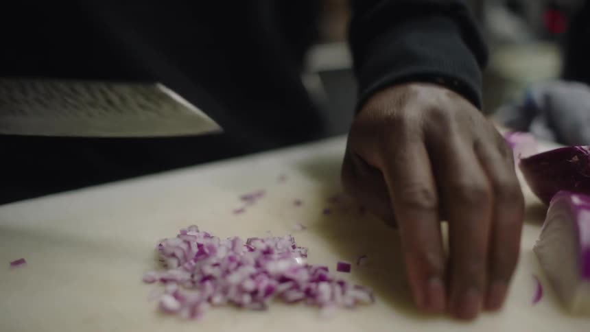 A person uses a knife to chop red onions on a large cutting board