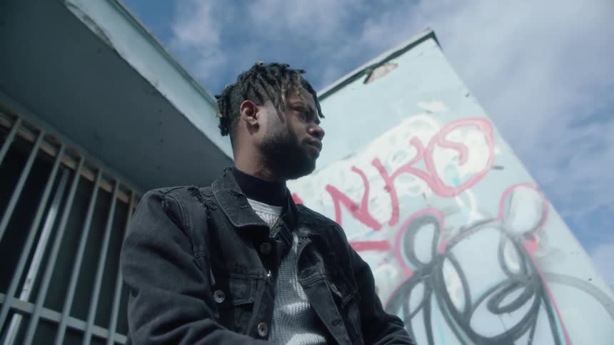 A black man sitting outside of a building looking around