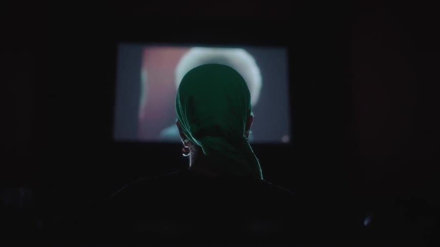 A person wearing an earring and a scarf on their head is watching a television in the darkness