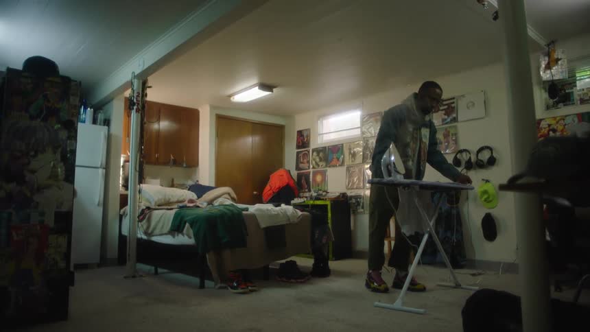 A man stands at an ironing board while ironing a plain white shirt