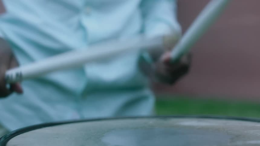 Man with white shirt plays drums using drumsticks