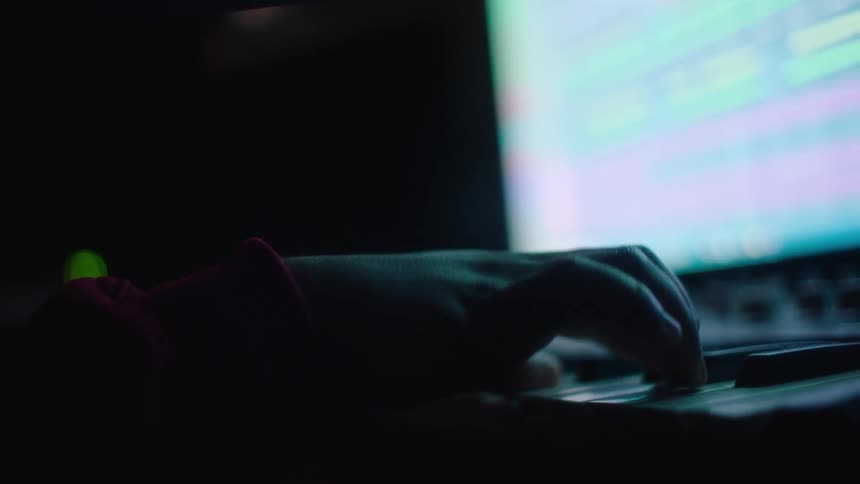 A musician is playing an electronic keyboard that is sitting near a computer monitor