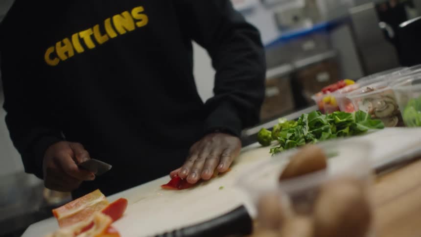 Man with black hoodie cuts red bell pepper with knife in the kitchen