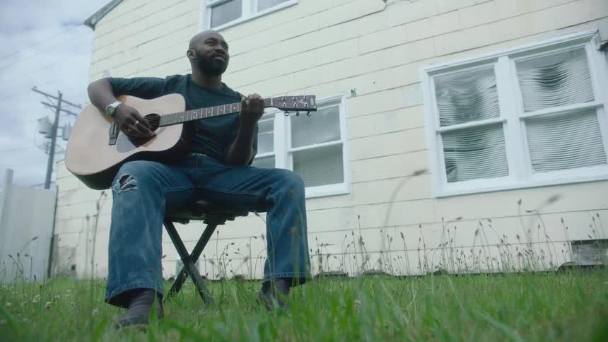 A man sits outside a house and plays guitar
