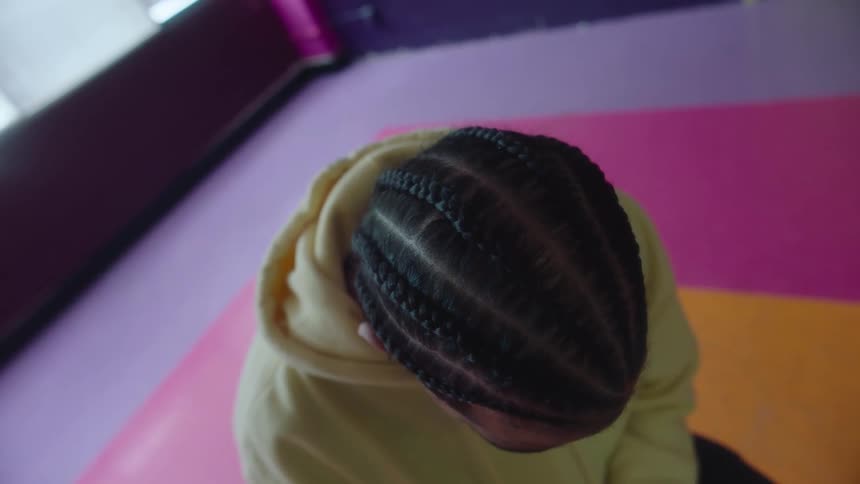 Person with dreadlocks and yellow hoodie looks down n pink orange floor