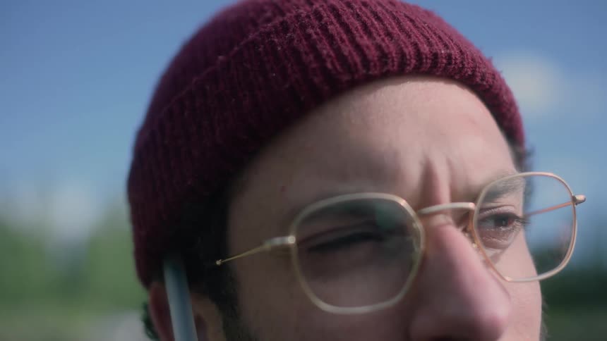 Man wearing knit hat and eyeglasses stands outdoors looking