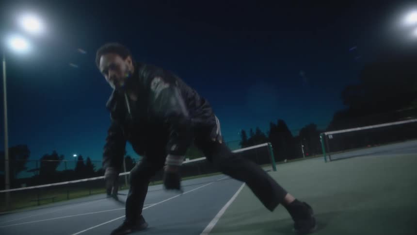 A man dancing outdoors on a tennis court