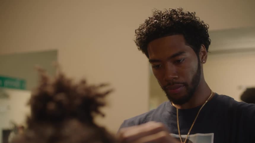 Barber with beard necklace and t shirt cuts persons hair in the barbershop