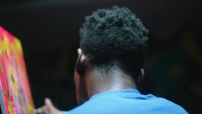 Back of the head of a man painting with oils on canvas inside a room