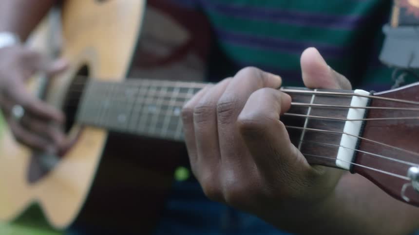 Close up of a young man playing acoustic guitar outdoors at daytime