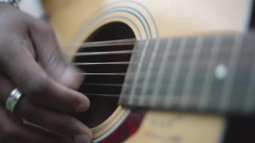 Young man plucking the strings of an acoustic guitar outdoors