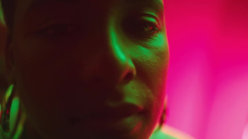 Close up of the face of a woman under colorful lights looking at the camera