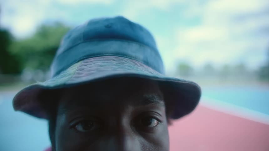 Man with blue hat looks up at camera on tennis court