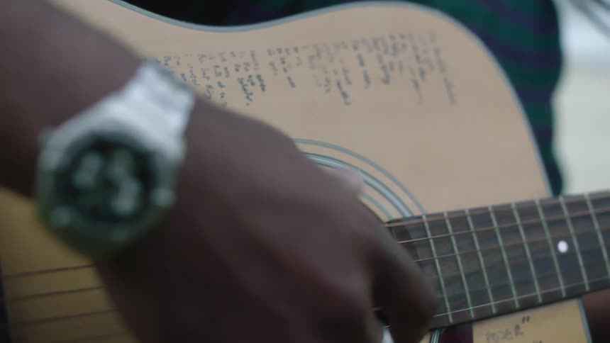 Musician strums acoustic guitar with words written on the wood